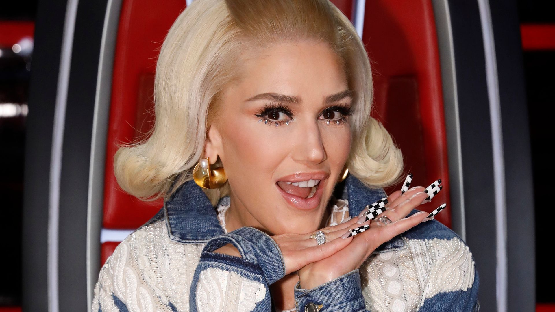 Gwen Stefani smiling at the camera sat in her coach chair on The Voice