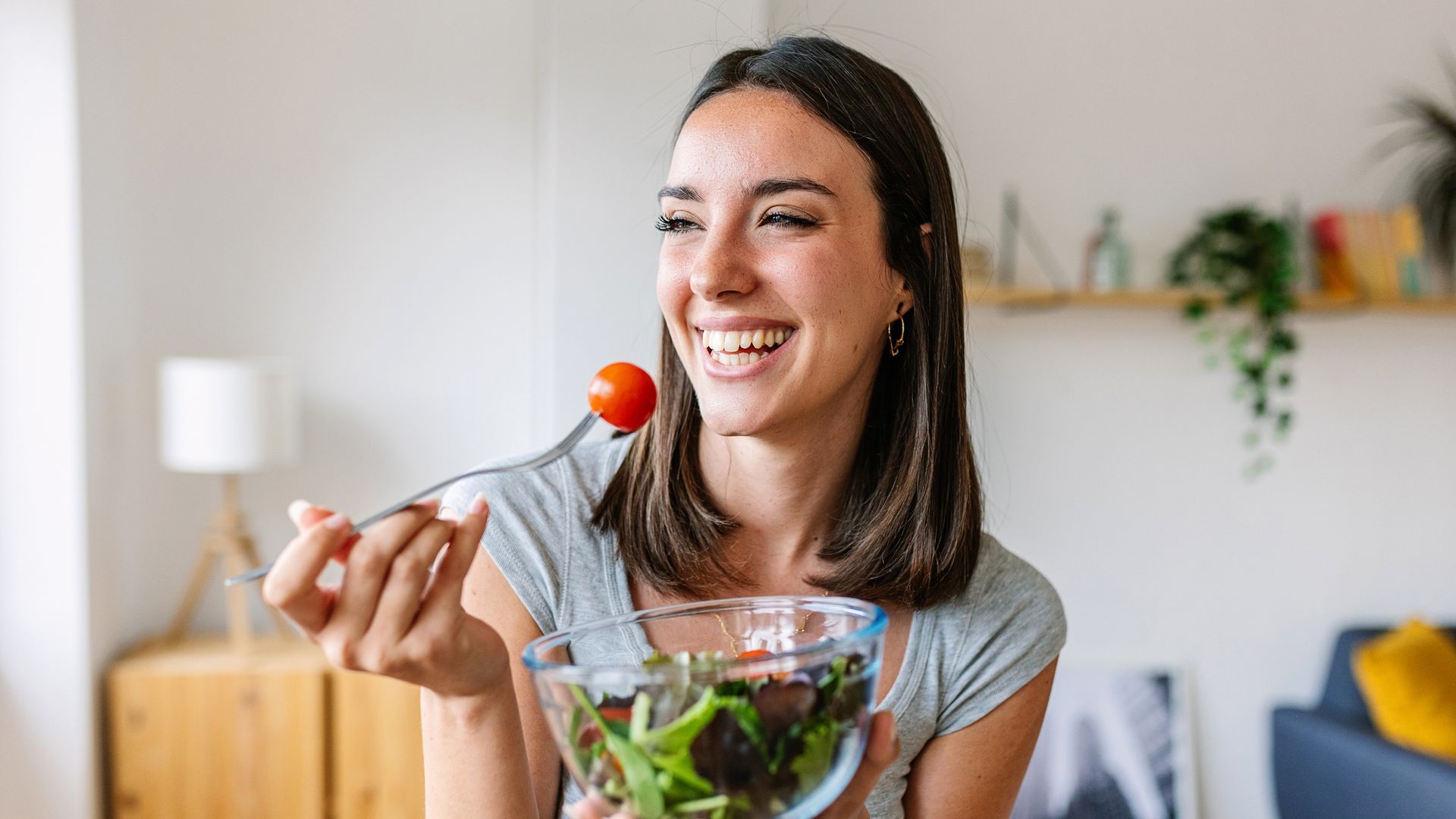 Happy young beautiful woman eating healthy green salad at home. Healthy lifestyle concept.