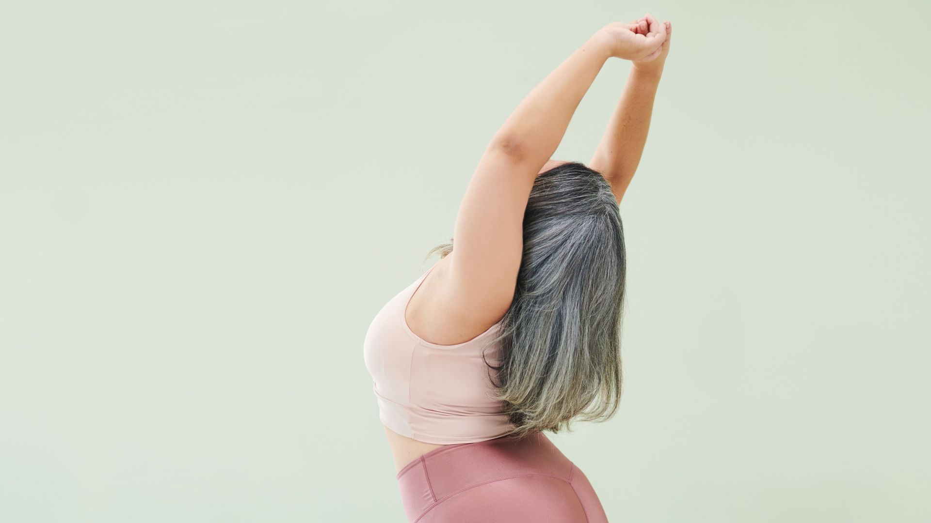Rear studio shot of an unrecognizable woman stretching against a green background