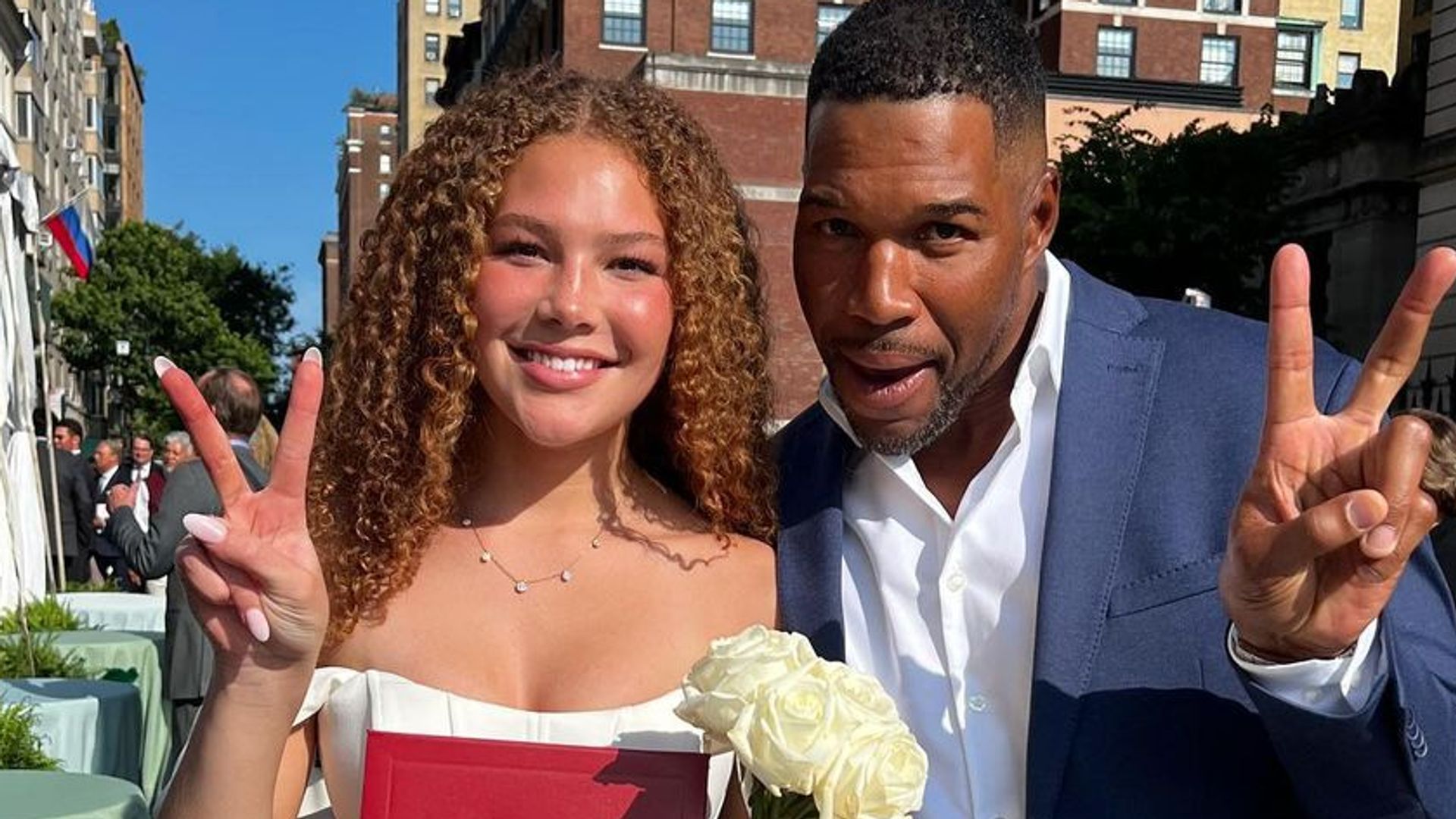 Michael Strahan in a blue suit making a peace sign with daughter Isabella