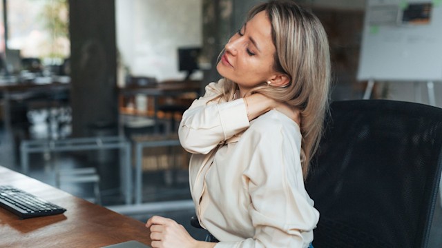 Businesswoman has stiffness in neck and shoulders from work at computer, tech neck or computer syndrome. Young female feeling under pressure, overworked spending long hours in office.