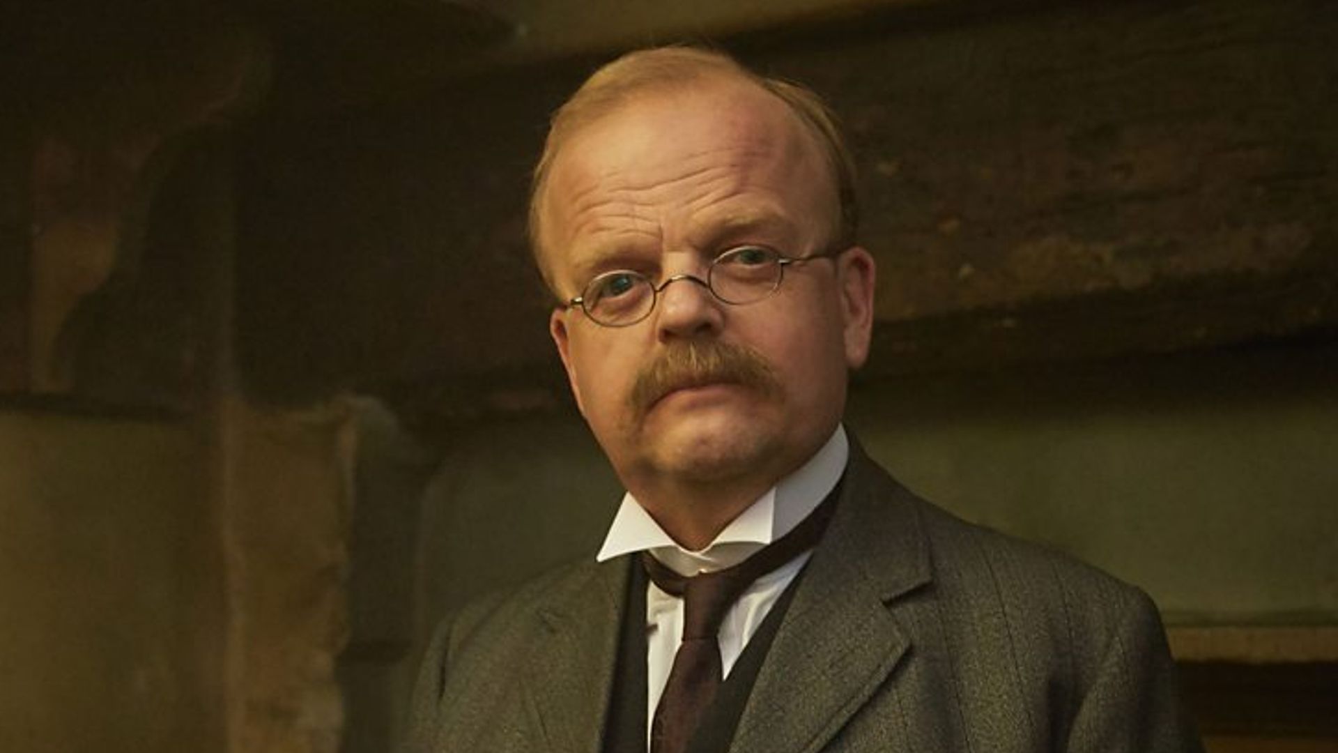 A man in period dress leans on a chair