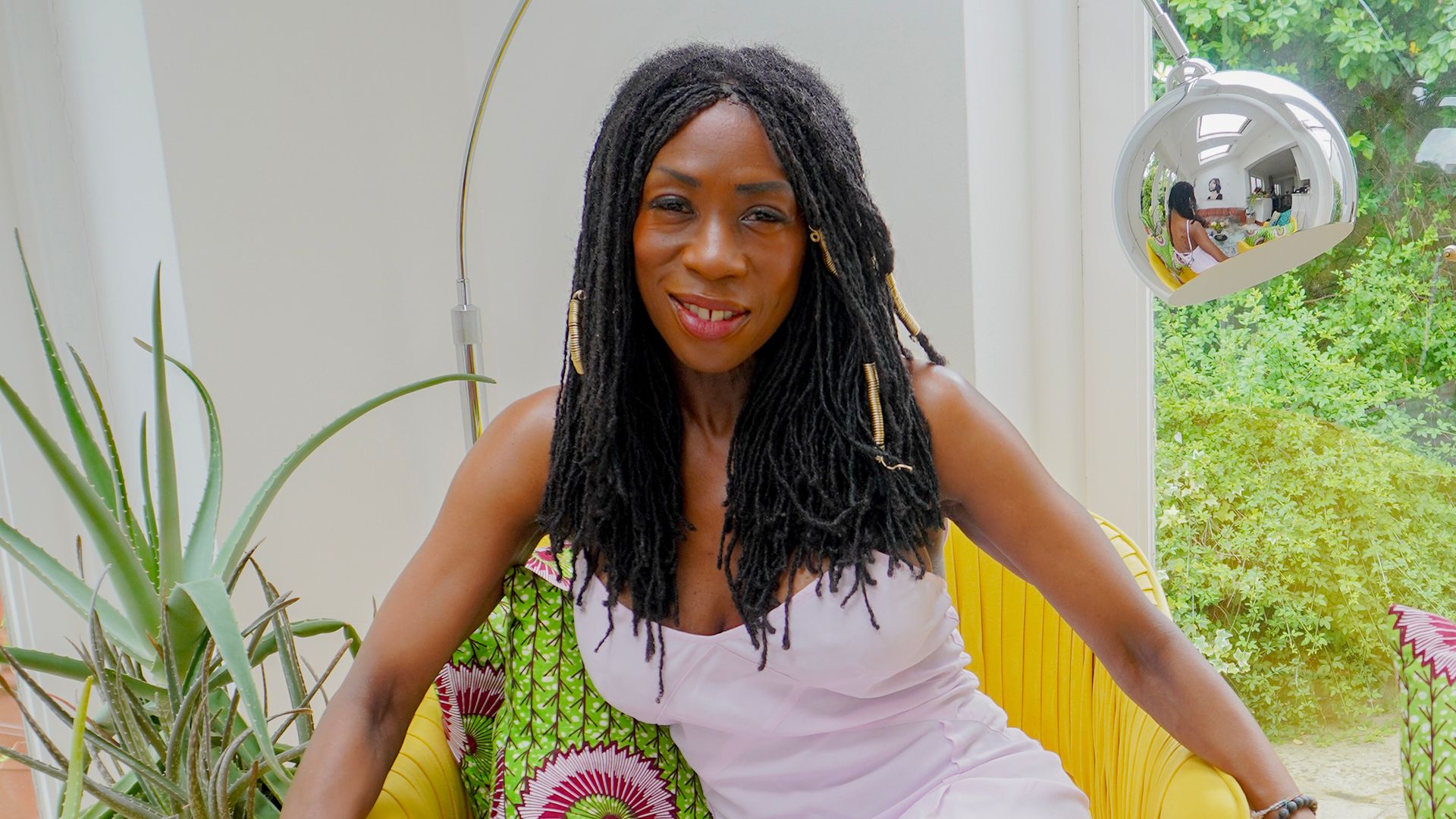 Heather Small in a dress sitting in a yellow chair