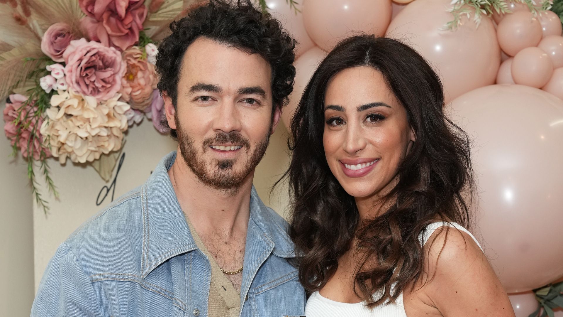 kevin jonas and danielle smiling for photo in front of pink balloon