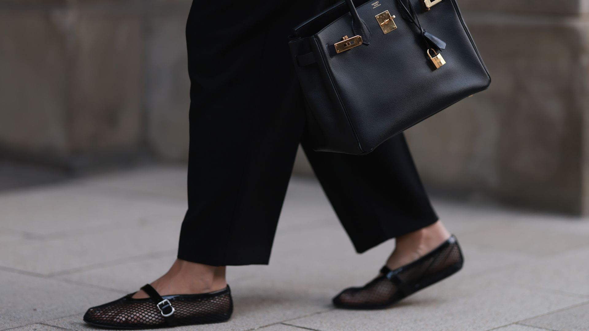 A person wearing black ballet flats carrying a Hermes bag