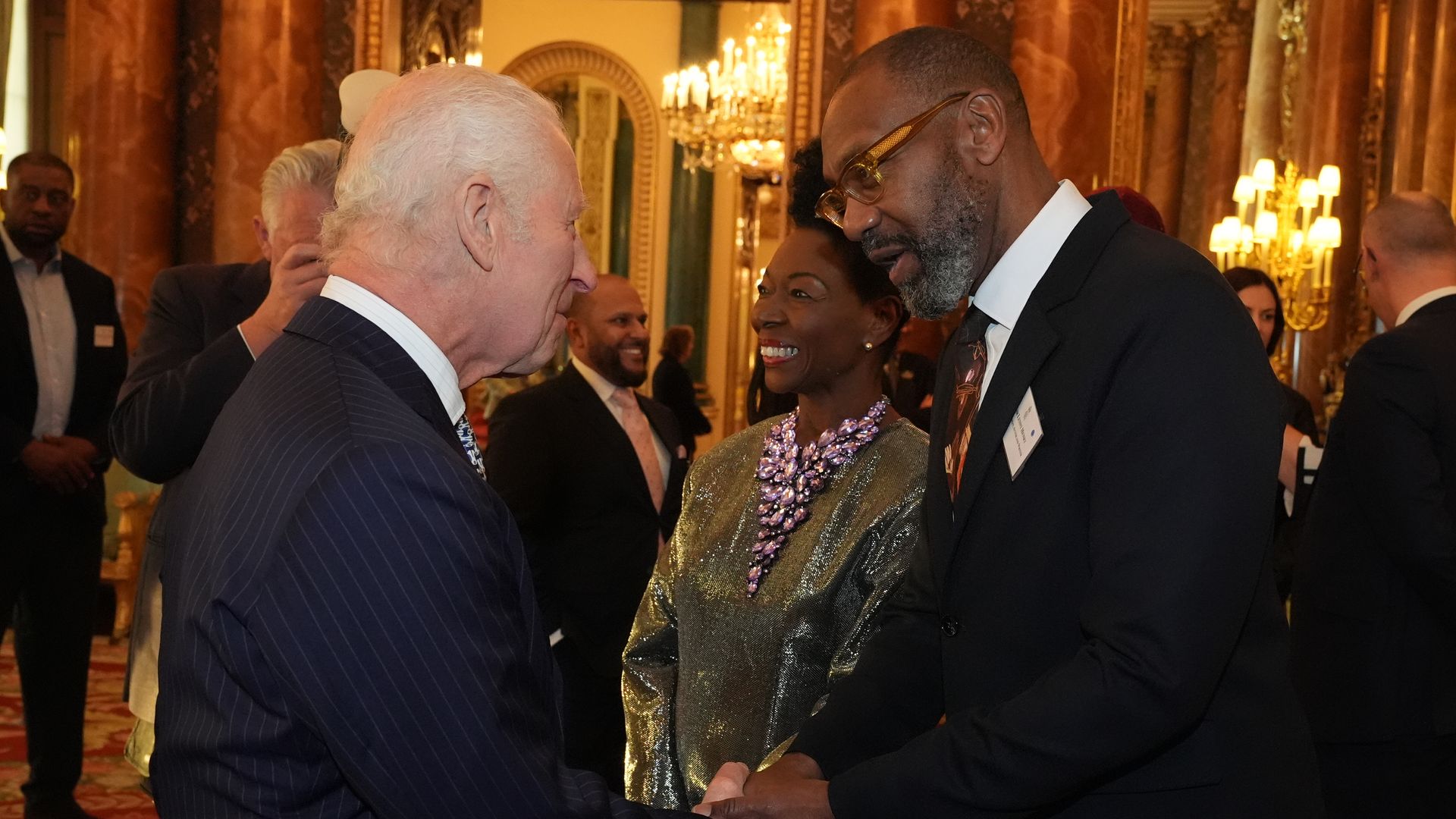 King Charles shaking hands with Lenny Henry; Floella Benjamin stands in the background