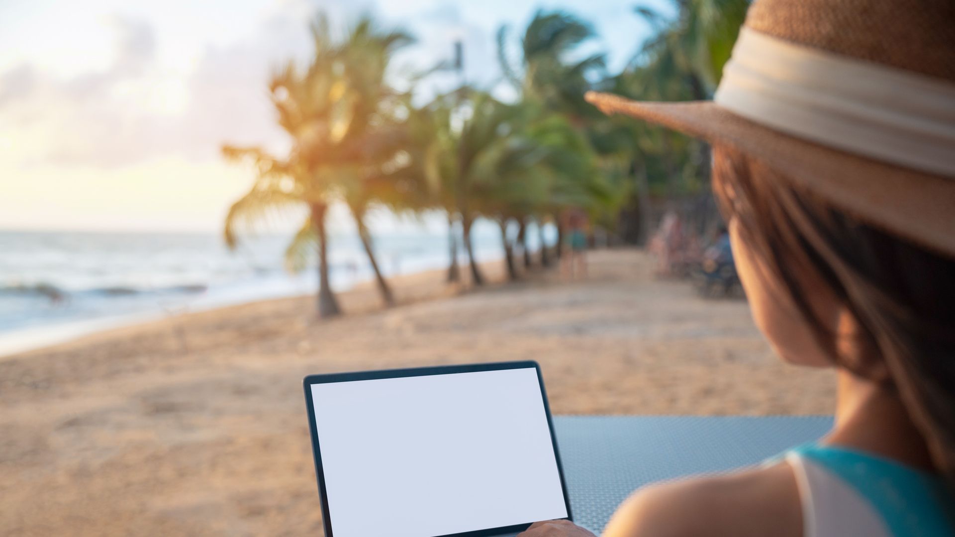 Business woman working with computer on the beach. Woman in a straw hat sitting in a deck chair on a beach types on her laptop