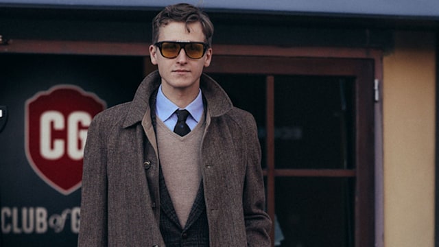 A guest outside Pitti Uomo in Florence wears a brown overcoat and suit combo