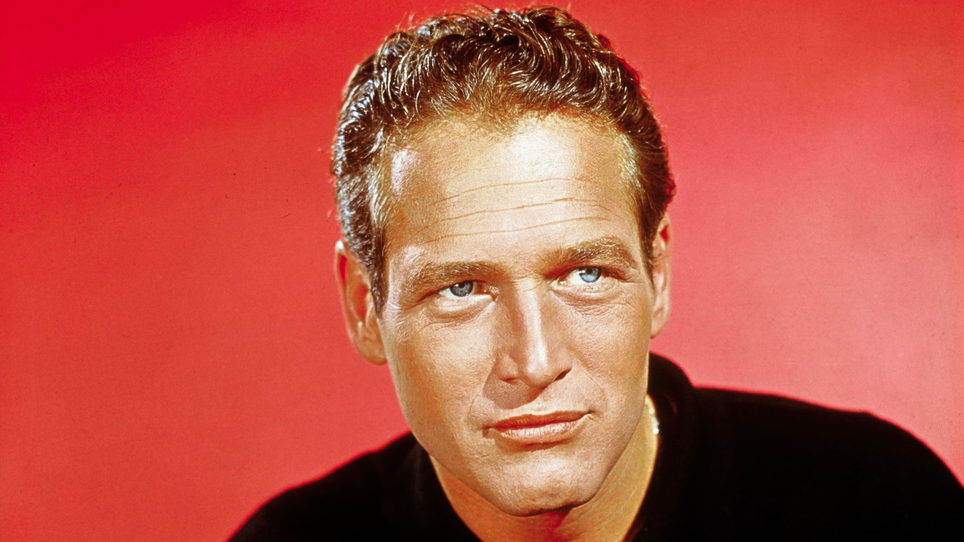 Close-up of Paul Newman wearing a black sweater. Red background.