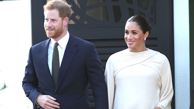 Prince Harry in a suit and pregnant Meghan Markle in a white dress