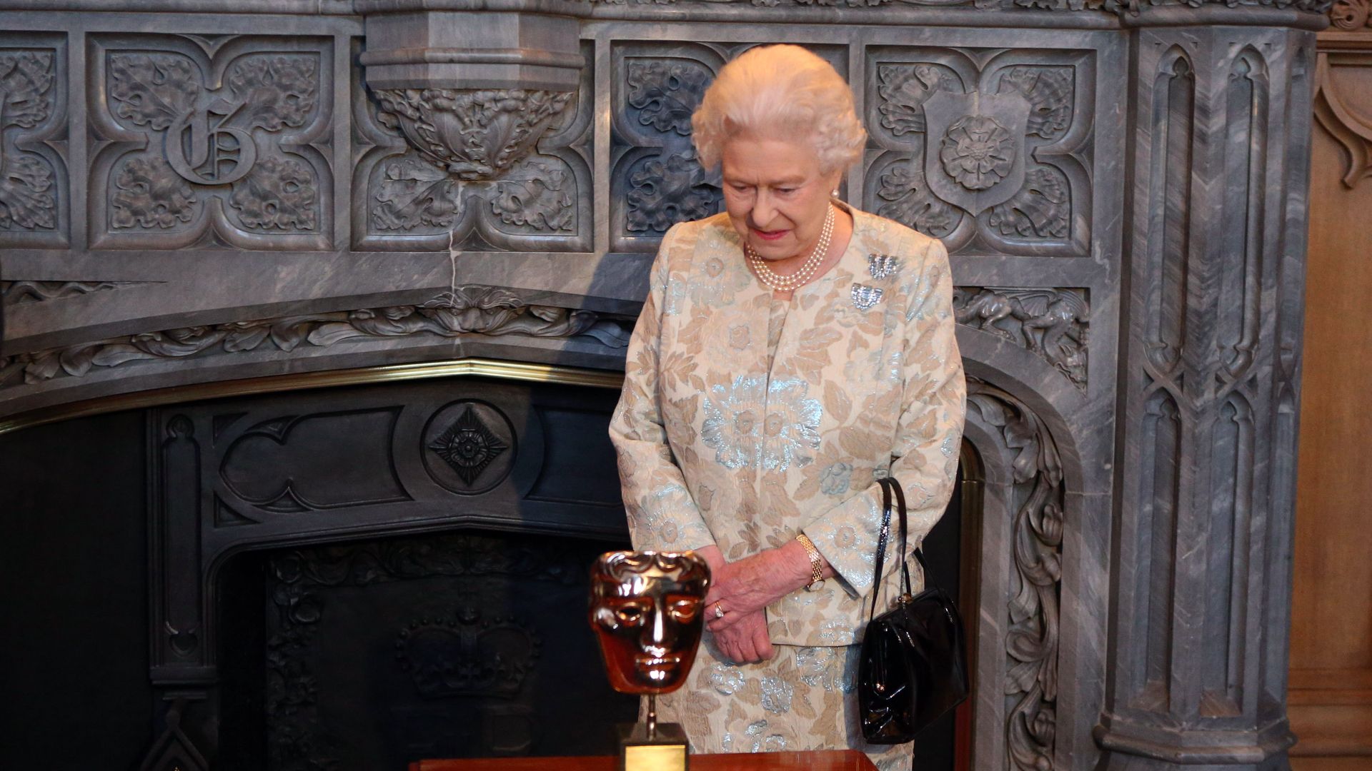 Queen Elizabeth II looks at the BAFTA that she received in recognition for a lifetime's support of British Film and Television at a reception for the British Film Industry at Windsor Castle on April 4, 2013 