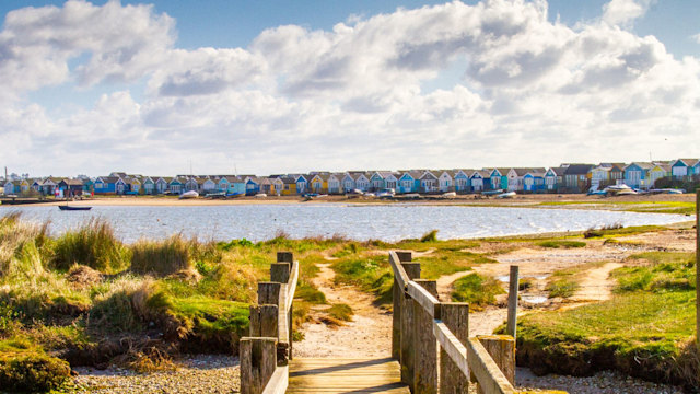 A bridge towards Mudeford Spit in Christchurch with coloured buildings on the beach