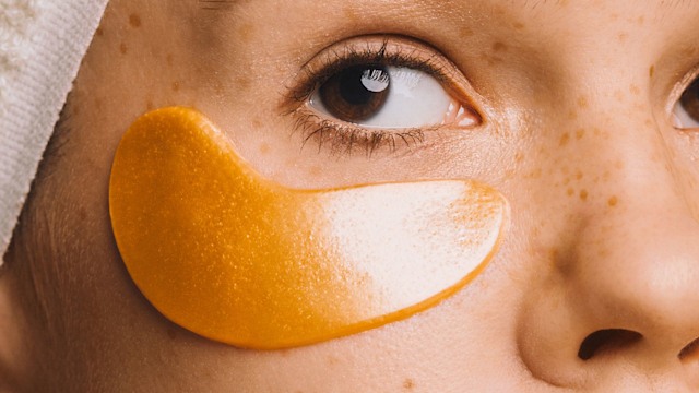 Girl in towel with gold-colored hyaluronic eye mask on her face