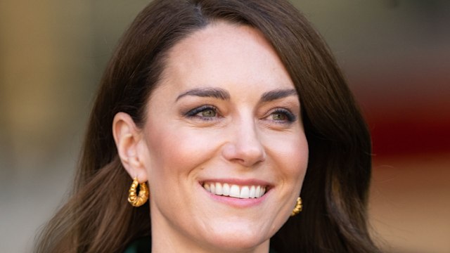 Kate smiling in green coat and gold earrings