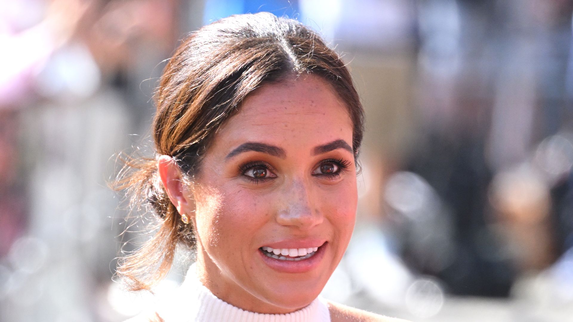 Meghan Markle looking animatedly in a white halterneck top
