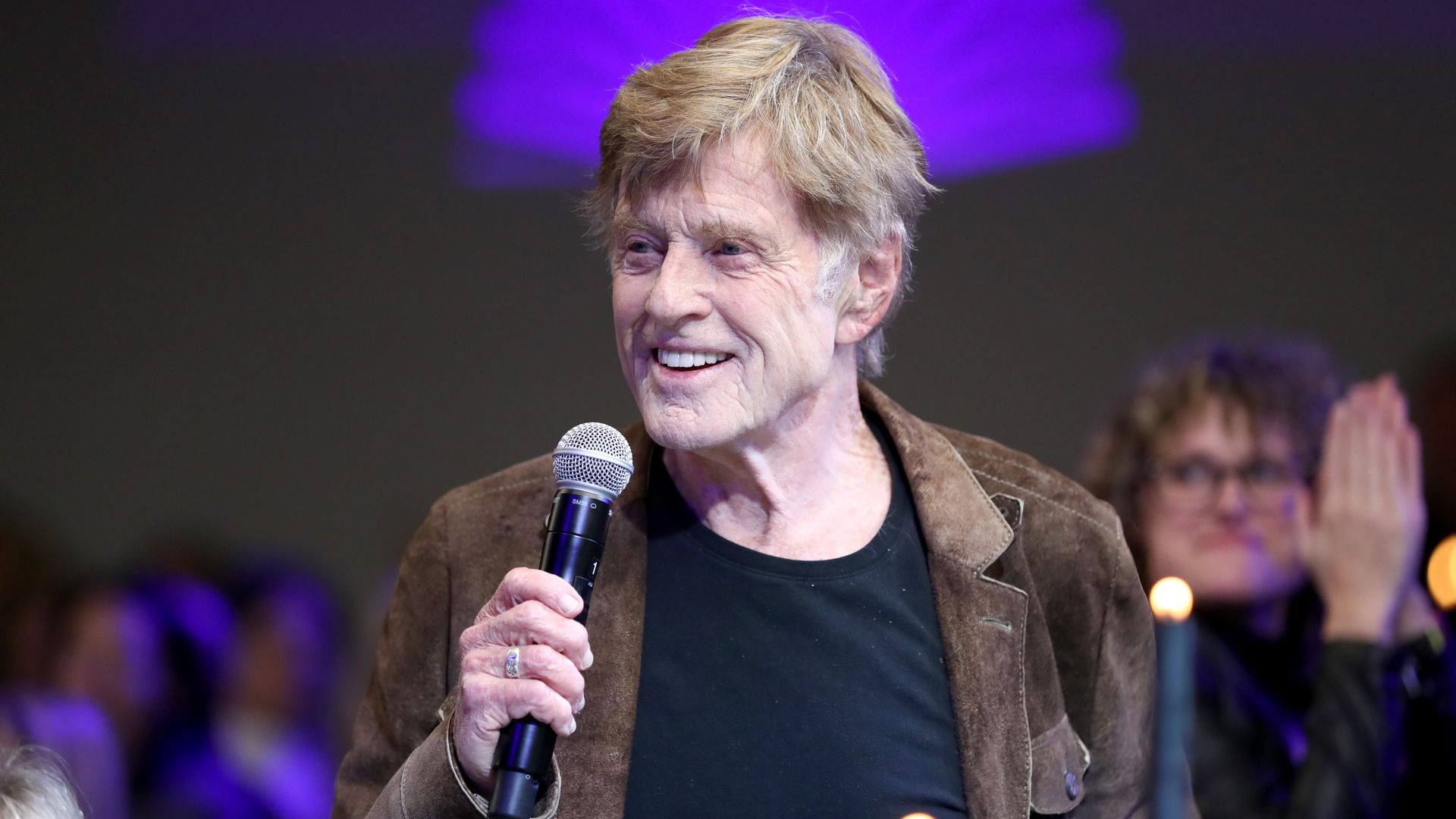 Robert Redford holding a mic and speaking to a crowd while smiling at Sundance Film Festival in 2020