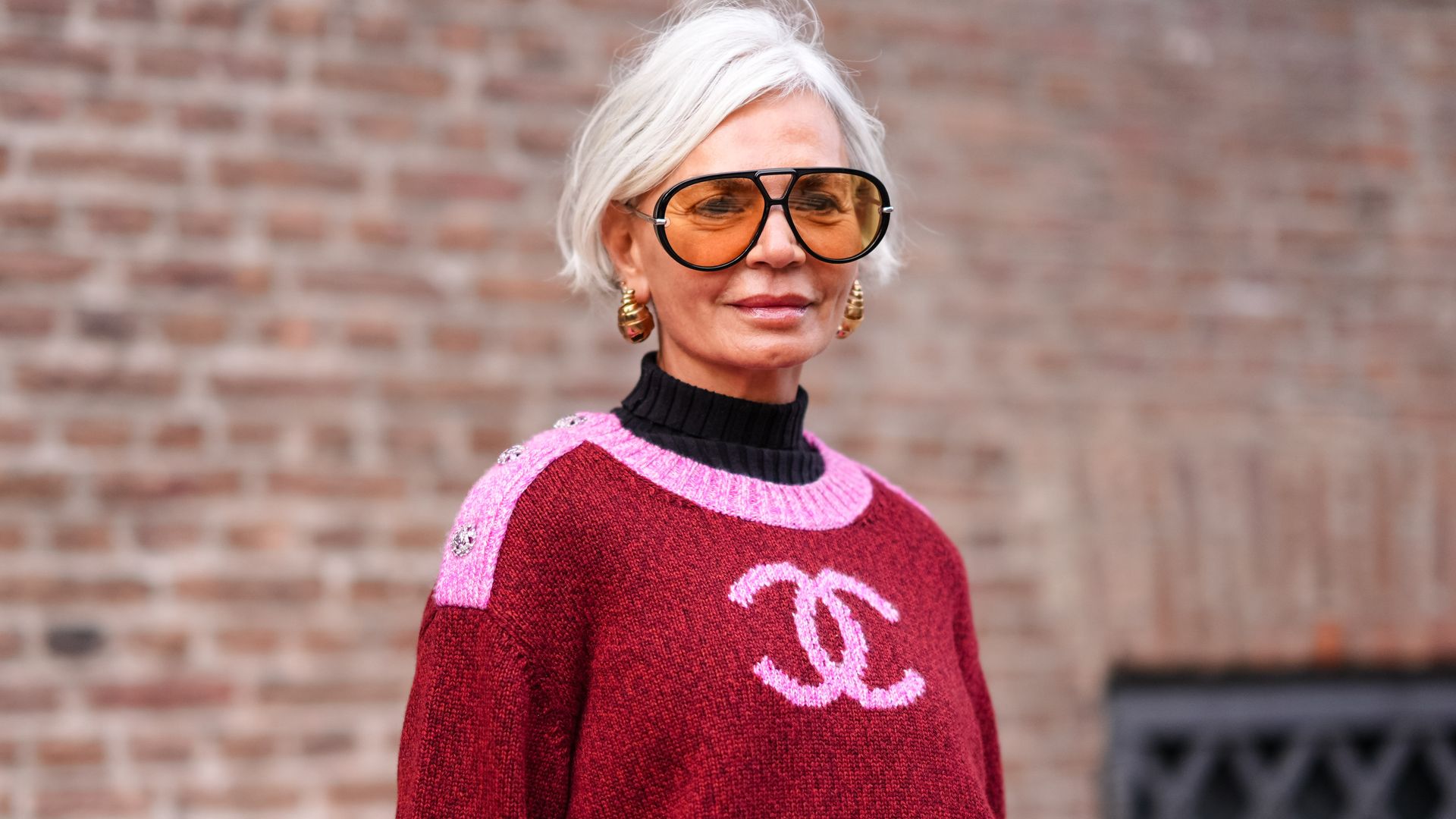 Grece Ghanem wears sunglasses, golden earrings, a black turtleneck pullover , a pink and red Chanel pullover, outside The Garment, during the Copenhagen Fashion Week AW24 on January 31, 2024 in Copenhagen, Denmark