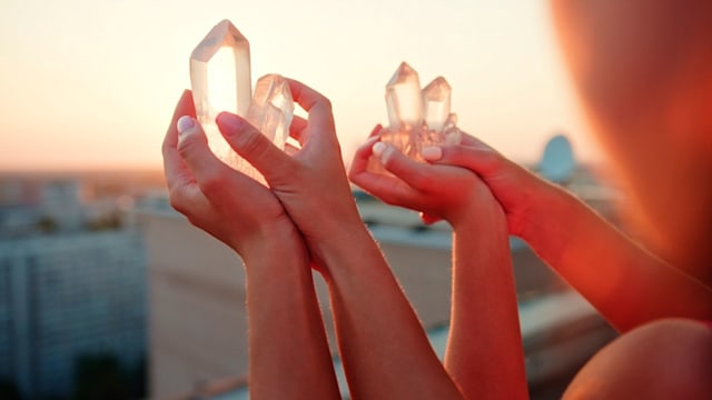 Two sisters holding healing crystals on of palm of their hands. Cityscape at sunset in background