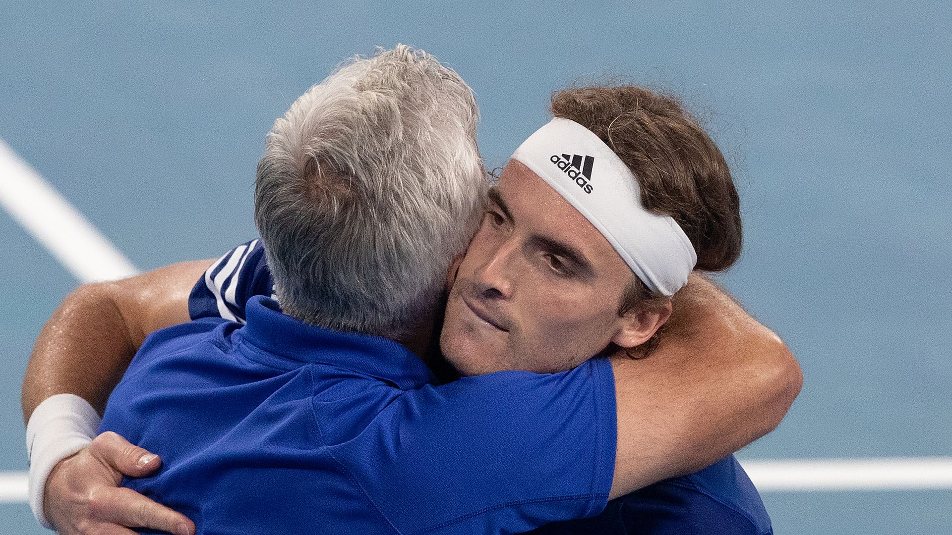 son and father hugging on tennis court