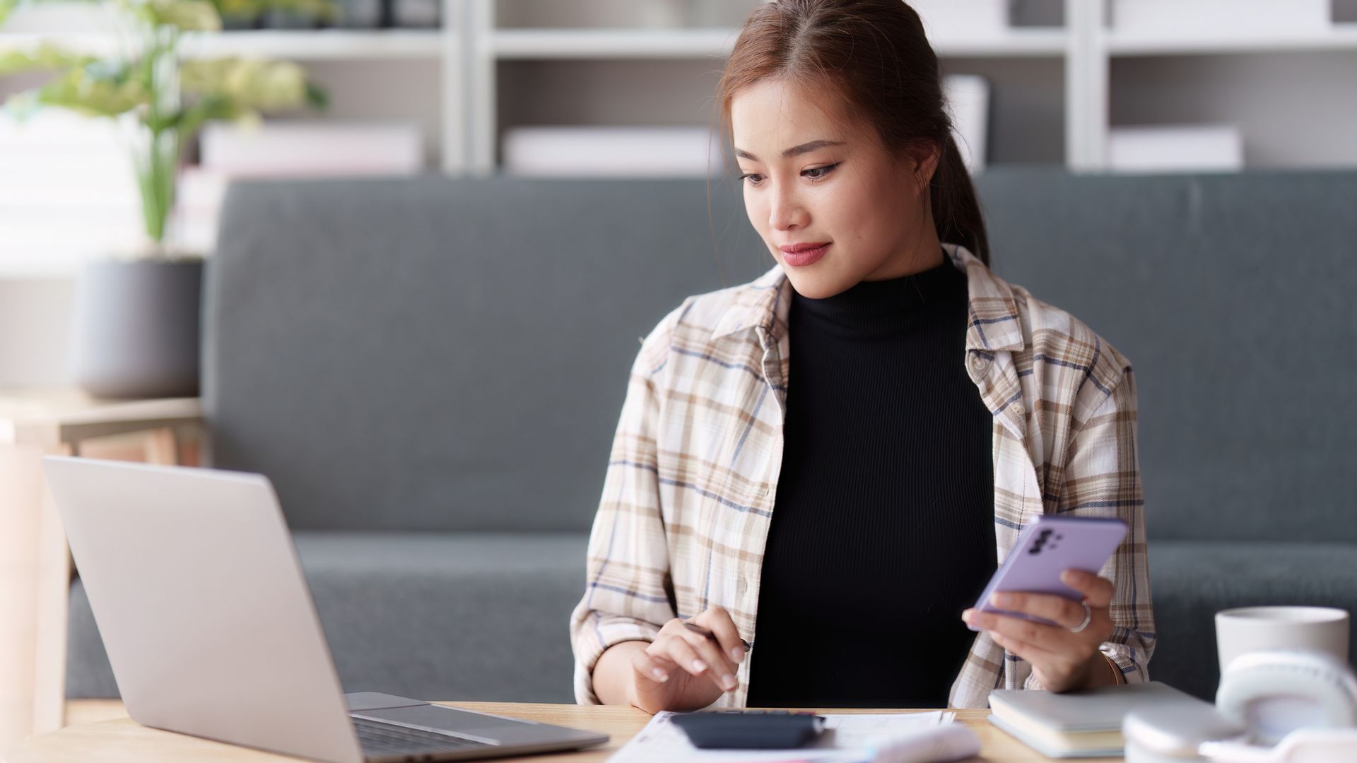 Woman typing on a calculator looking at her laptop