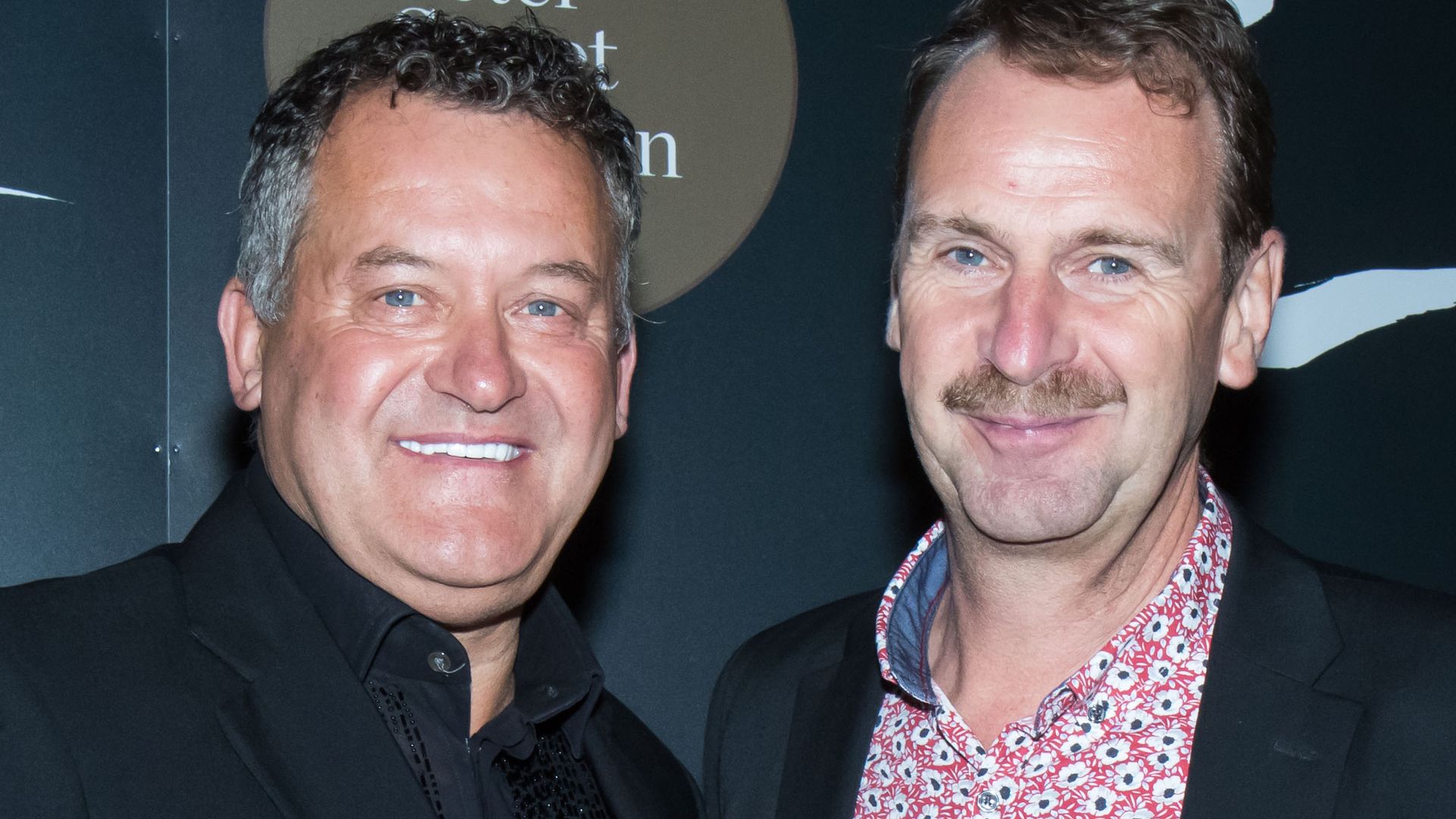 Paul Burrell in a black jacket and his husband Graham Cooper in a pink floral shirt