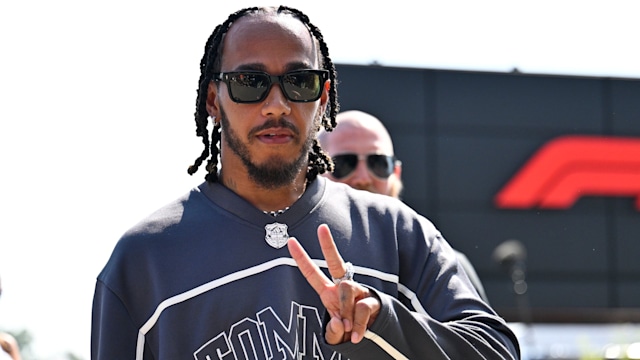 Lewis Hamilton in a grey jumper flashing a peace sign with his tongue sticking out