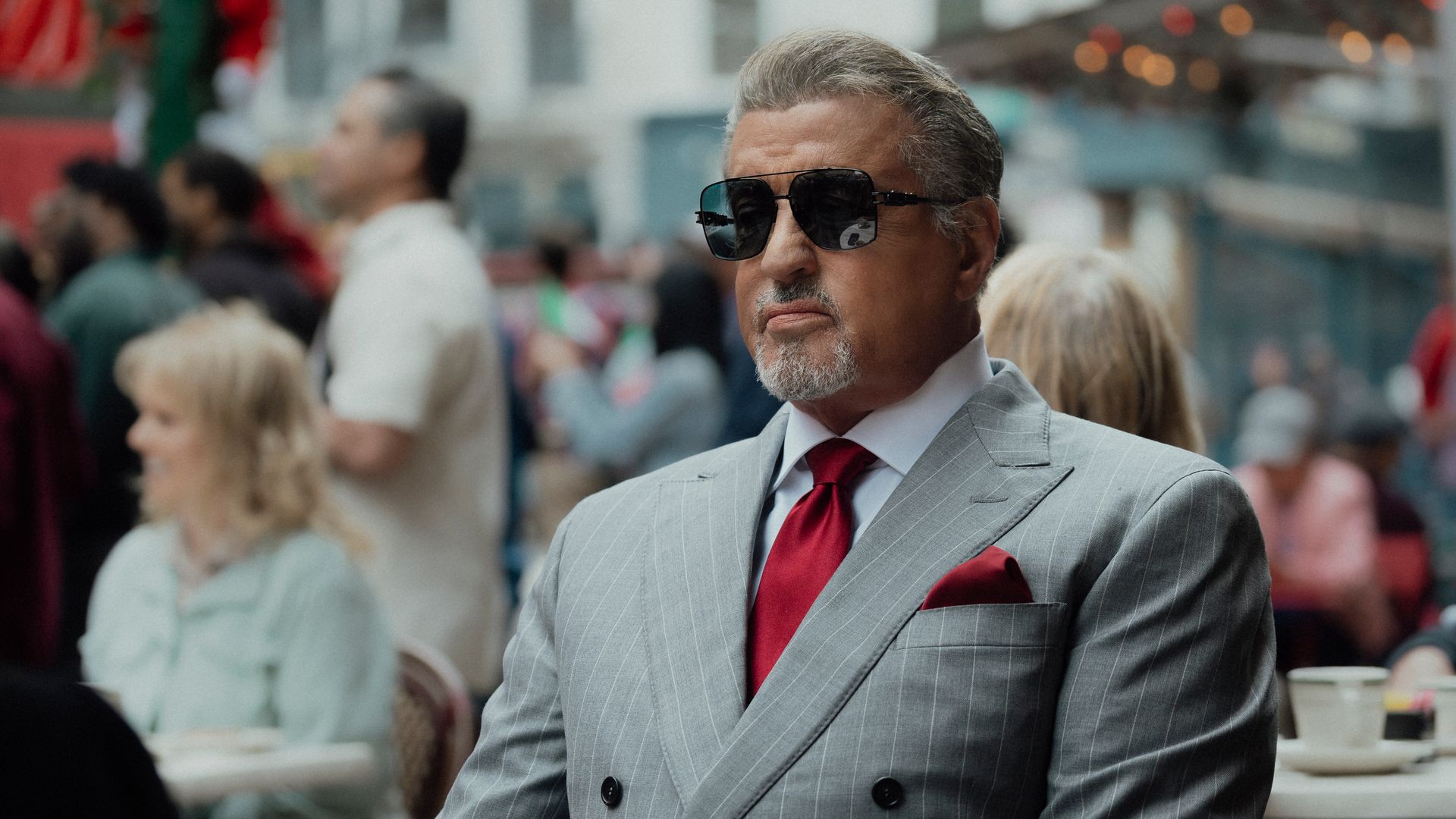 man in grey suit and glasses sitting at cafe table outdoors
