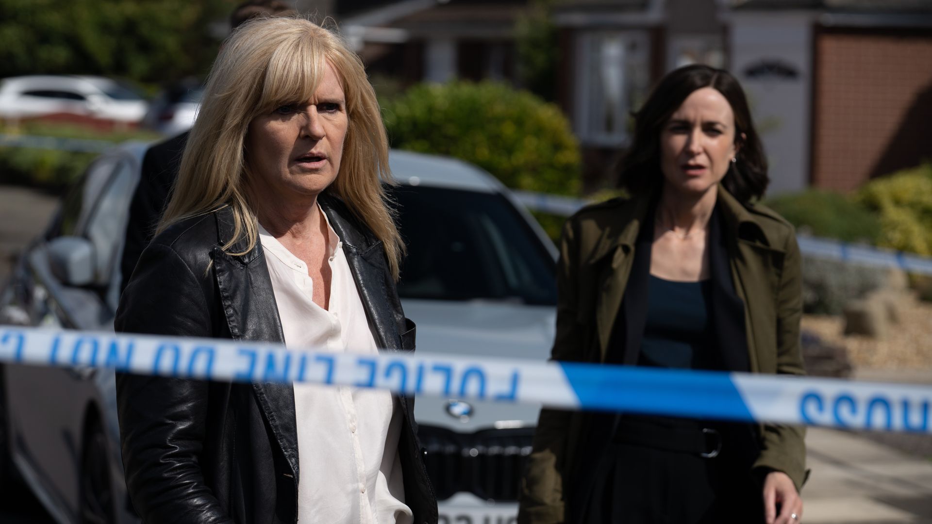 Two women standing behind blue police tape