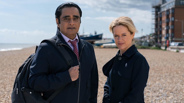 Two detectives standing on beach looking into camera