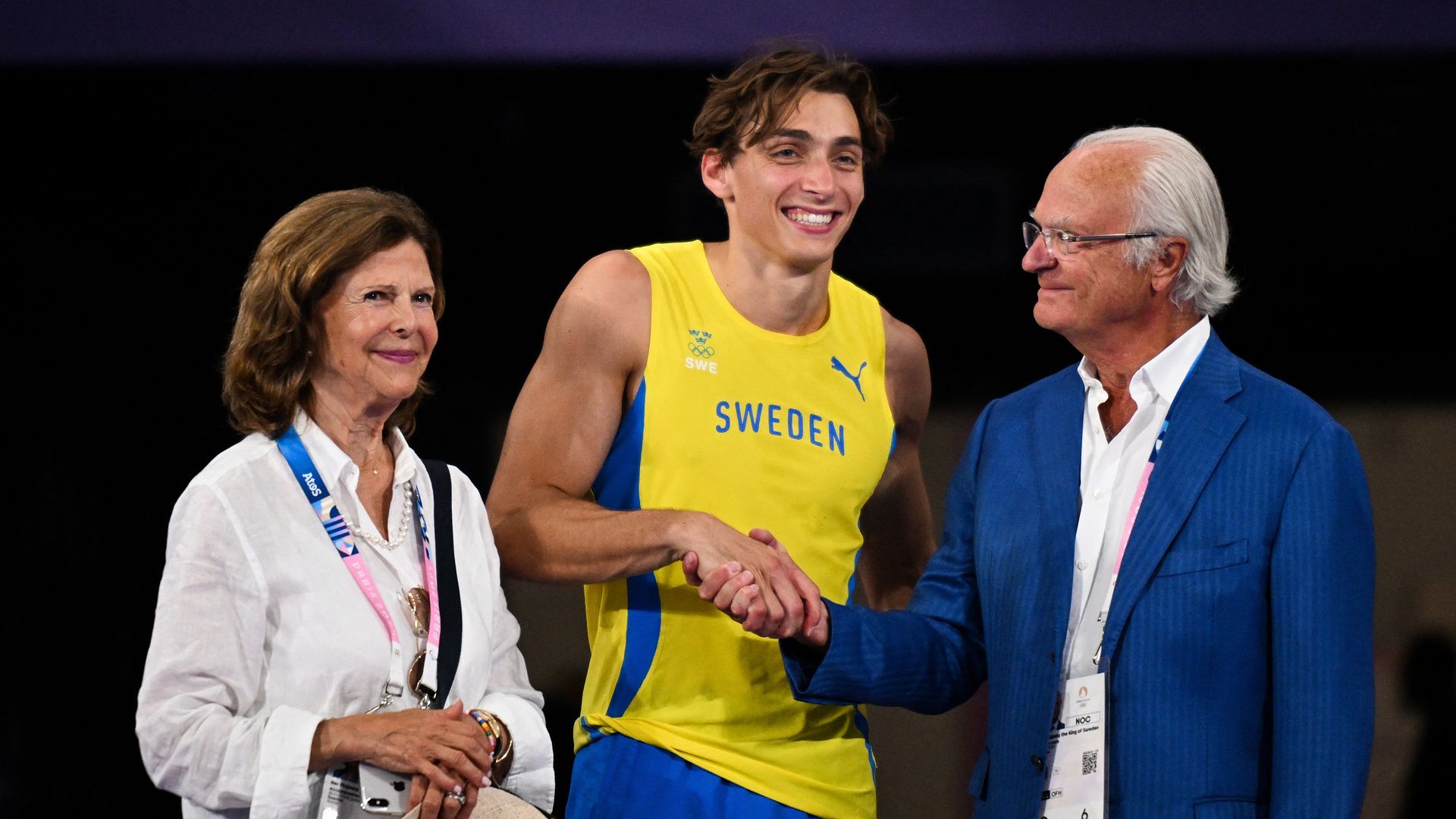 Queen Silvia standing with Armand Duplantis as he shakes King Carl Gustaf's hand