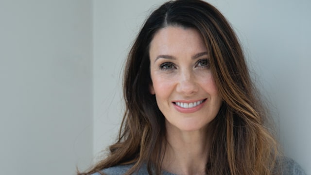 Woman smiling in grey jumper and jeans