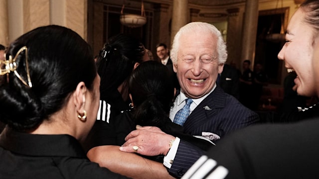 Britain's King Charles III reacts as he is hugged by members of New Zealand's Black Ferns rugby union team,