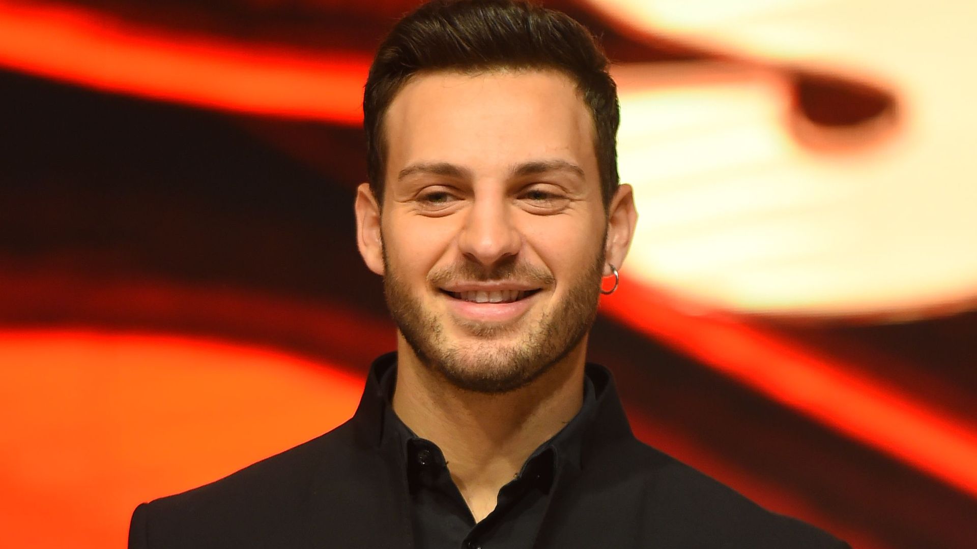 Vito Coppola smiling in a black suit against a red background