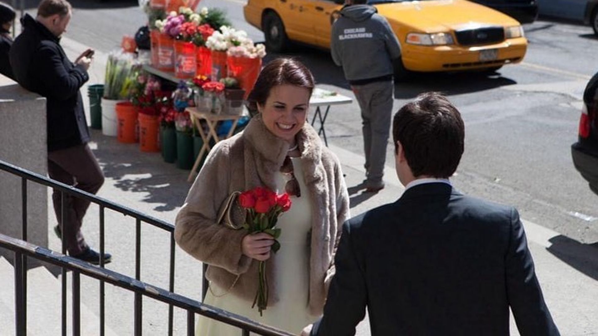 Nina Warhurst holding red roses and wearing a white dress and fur coat on her wedding day in New York