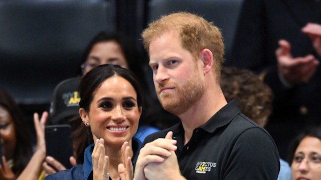 Meghan Markle clapping next to a grumpy(ish) Prince Harry