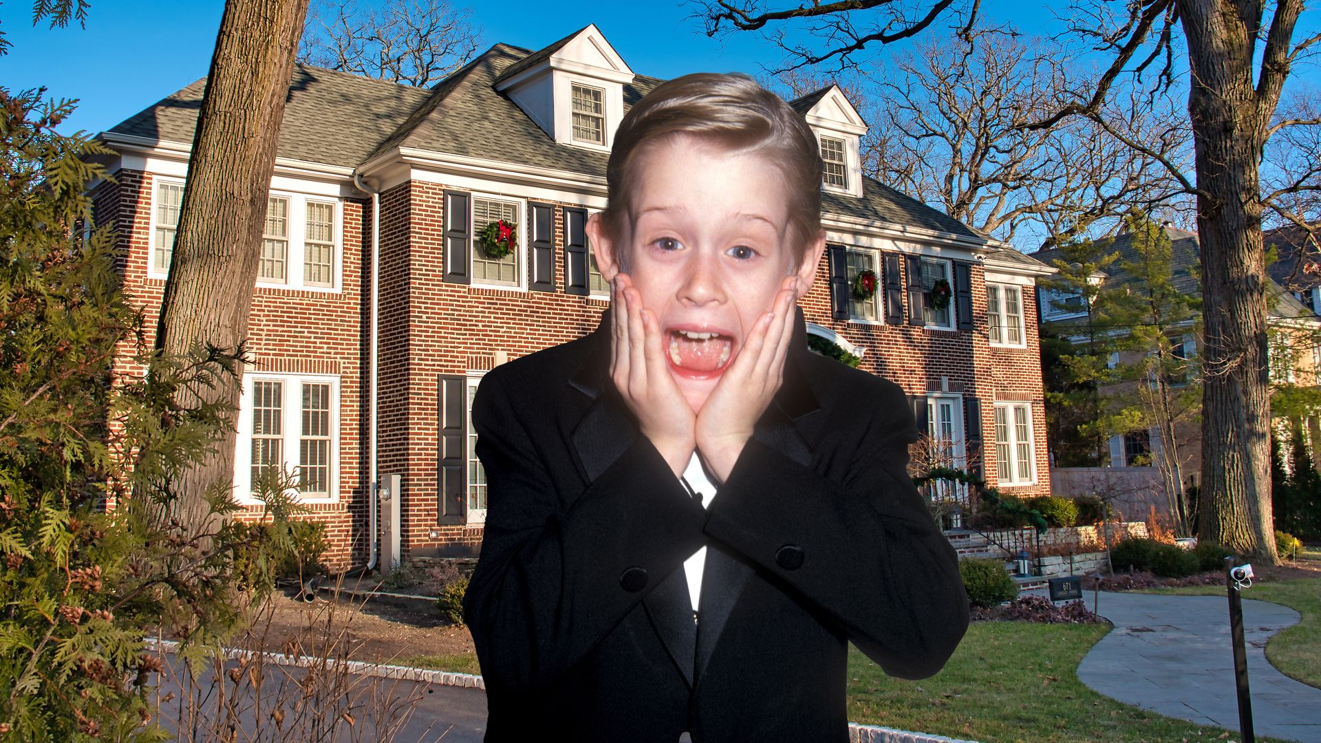 Mccauley Culkin in a suit doing his signature pose in front of the home alone house