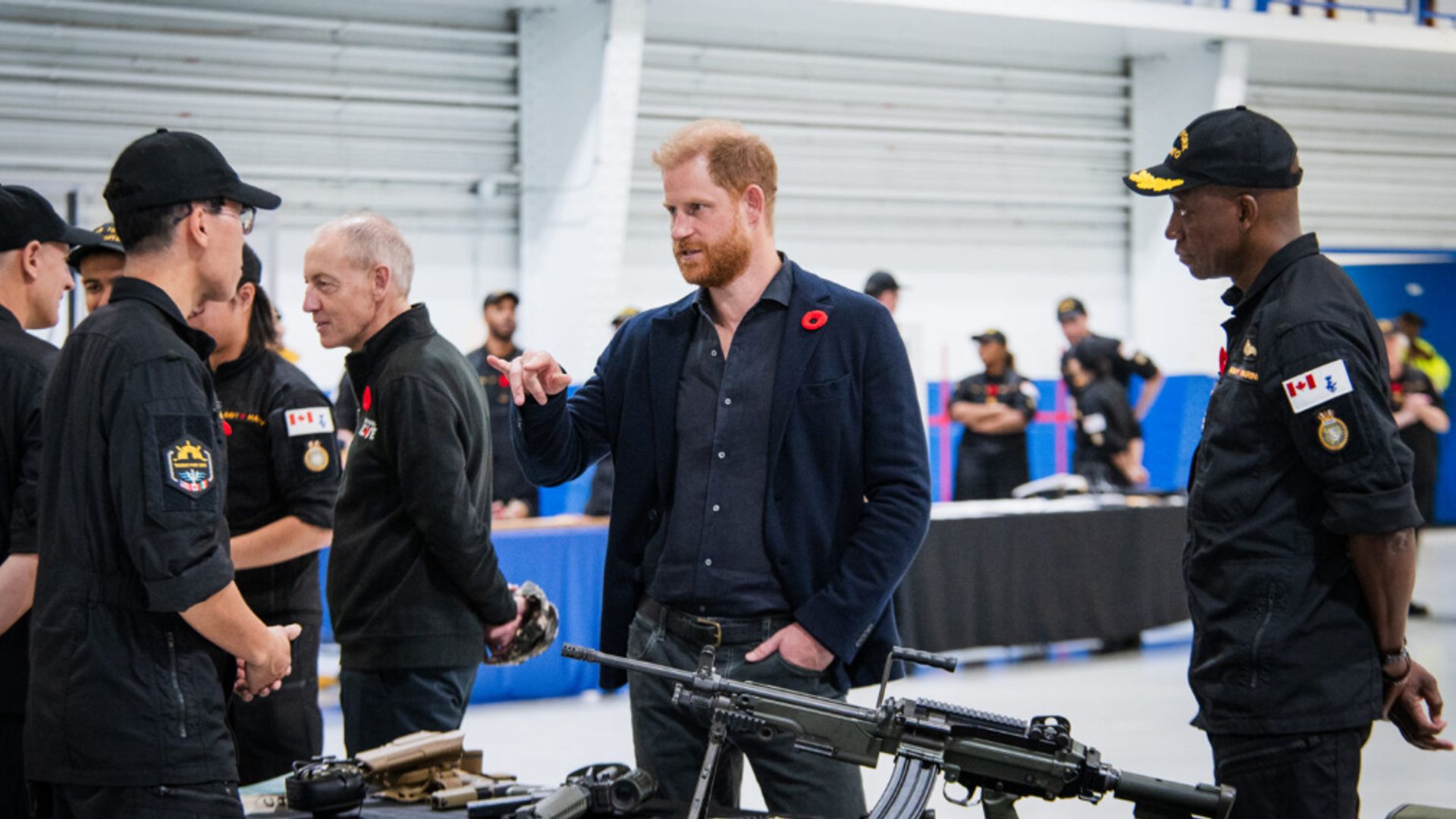 Prince Harry speaking to military personel, a gun is in front of him