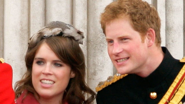 Princess Eugenie in a red jacket and Prince Harry in his black uniform stand on the balcony of Buckingham Palace