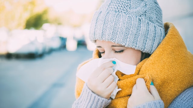 A woman with a cold blows her nose 