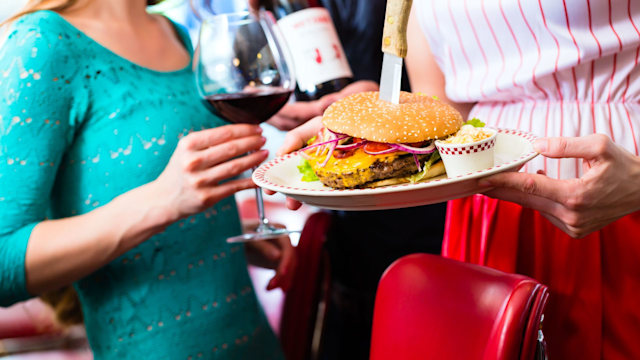 Friends or couple eating fast food in American fast food diner, the waitress serving the food, burgers, fries, and red wine