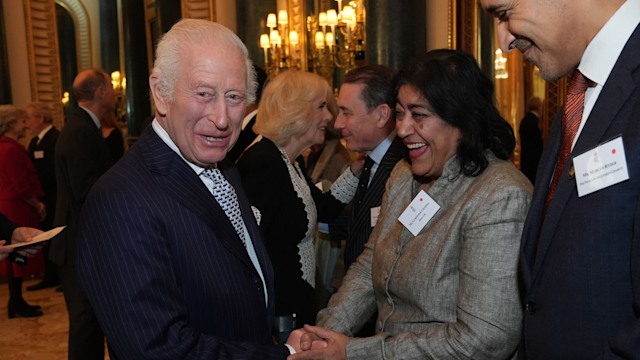 King Charles laughing with Gurinder Chahdam with Queen Camilla in the background