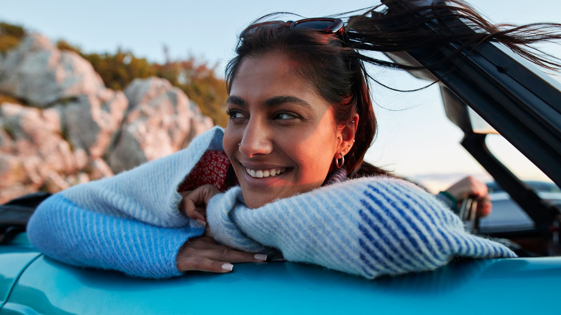 Smiling young woman day dreaming while leaning on convertible car during road trip