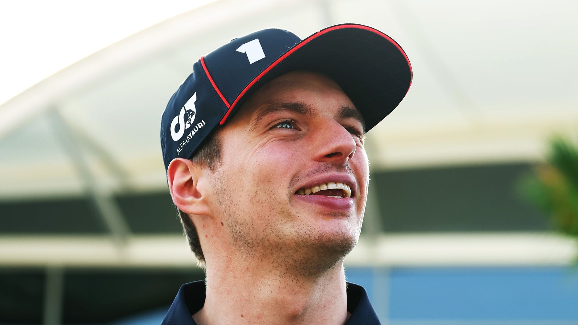 Max Verstappen in a Red Bull team outfit looking up and smiling