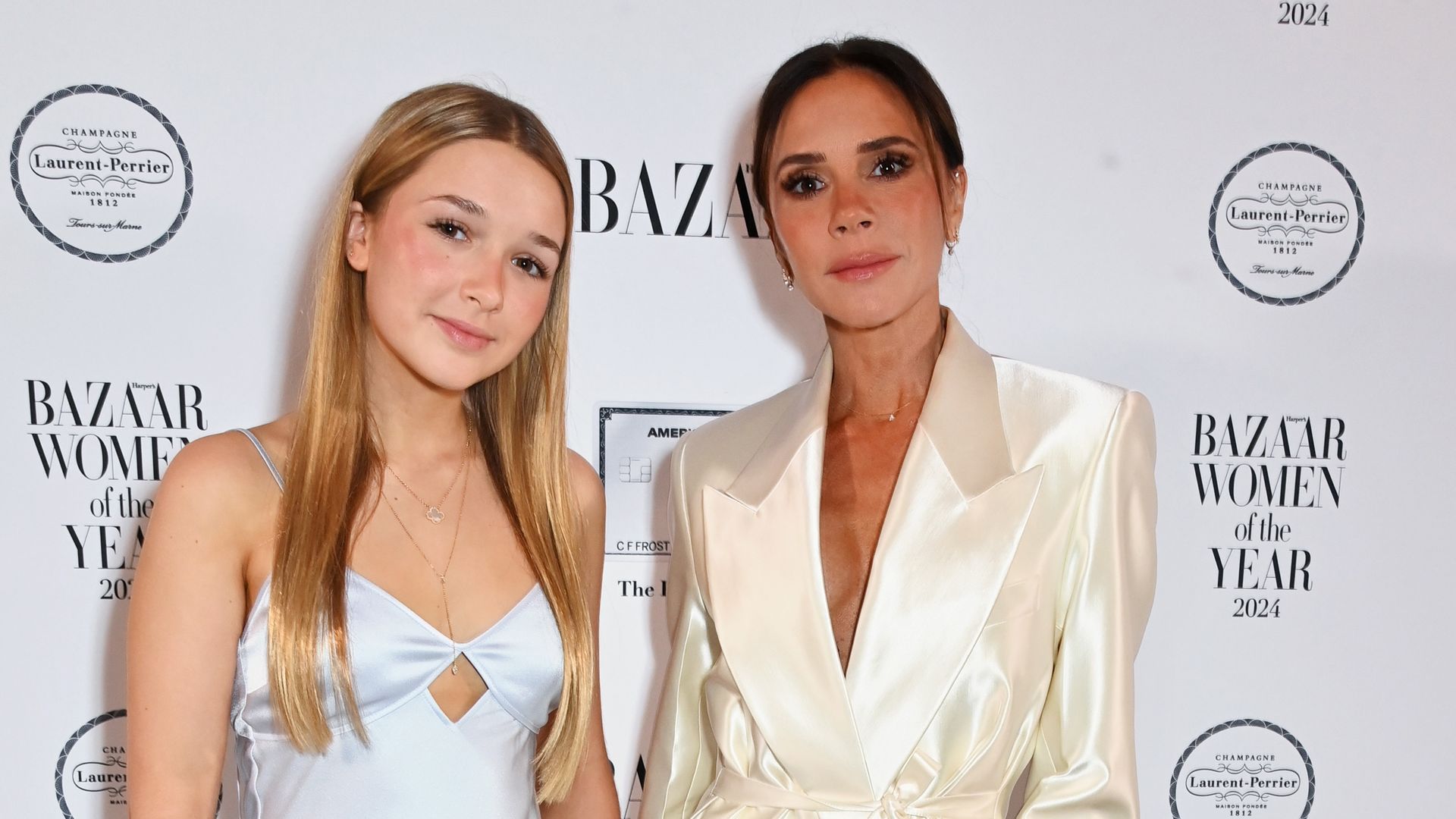 Harper and Victoria Beckham pose on the red carpet, Harper wears a long white slip dress and Victoria a silky blazer and matching trousers