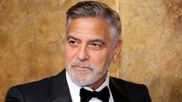 George Clooney wearing a tuxedo in front of a gold background posing for photographers at charity event in 2023