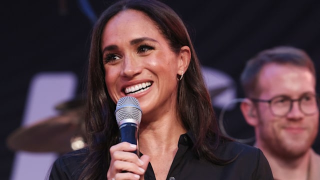 Meghan wearing black dress and holding a microphone