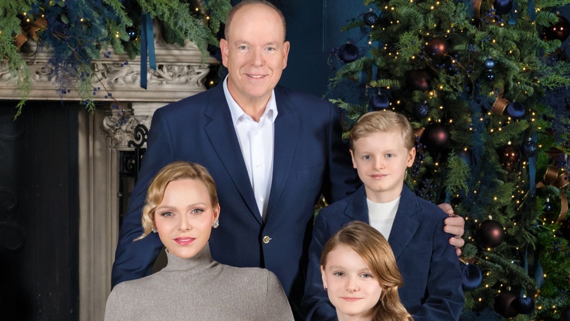 prince albert, princess charlene and two children pose in front of christmas tree and fireplace