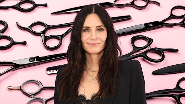 Courteney Cox in black blazer with hairdressing scissors backdrop