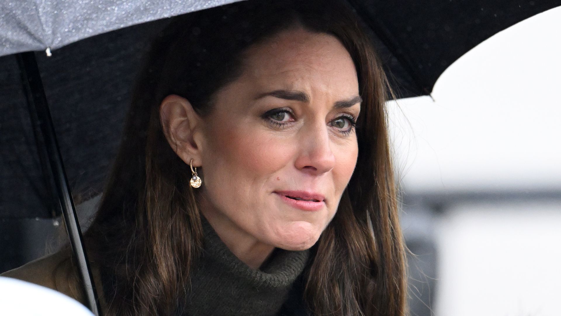 Princess Kate looking worried under an umbrella