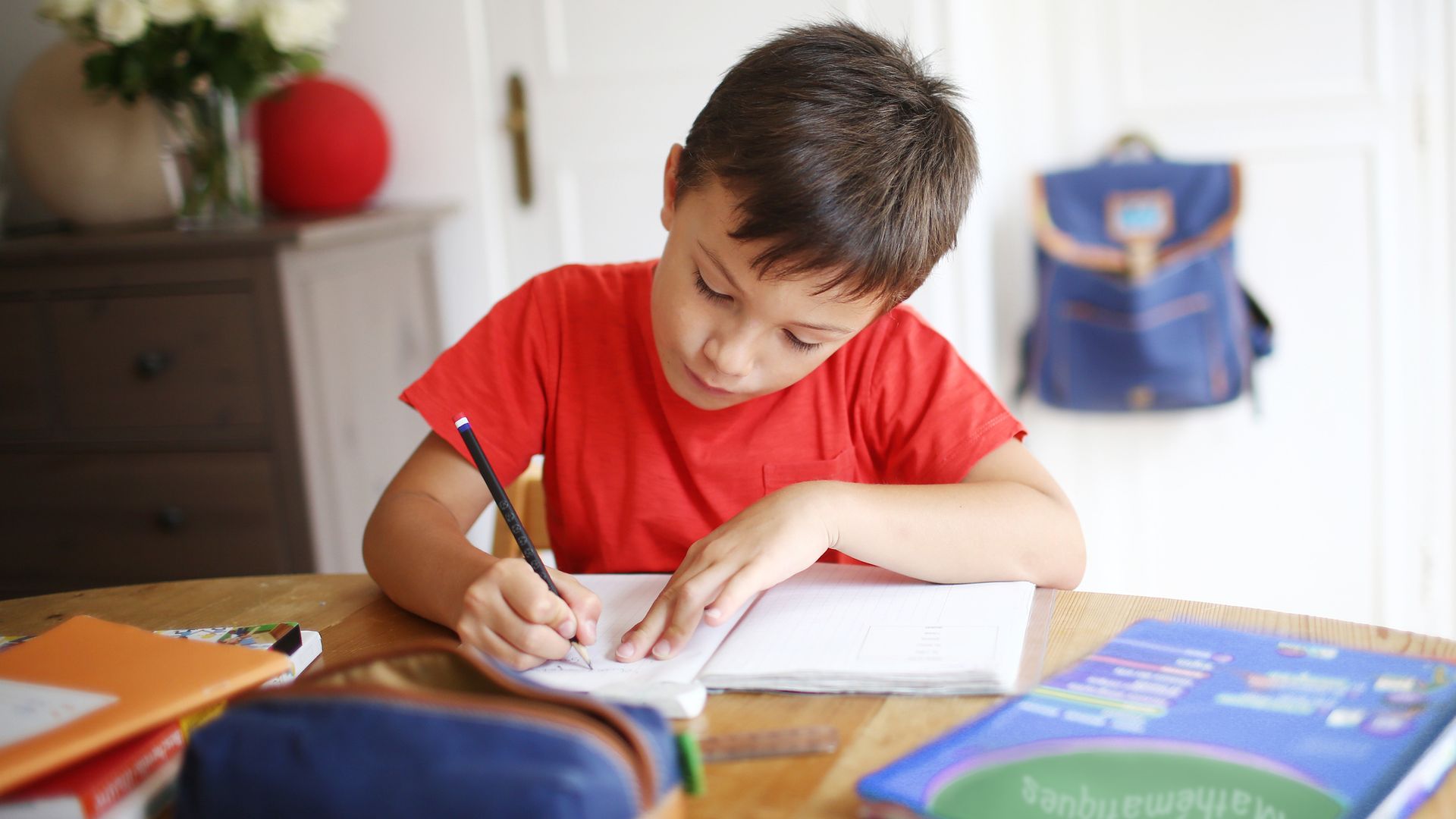 A 7 years old boy doing his homework in red t-shirt
